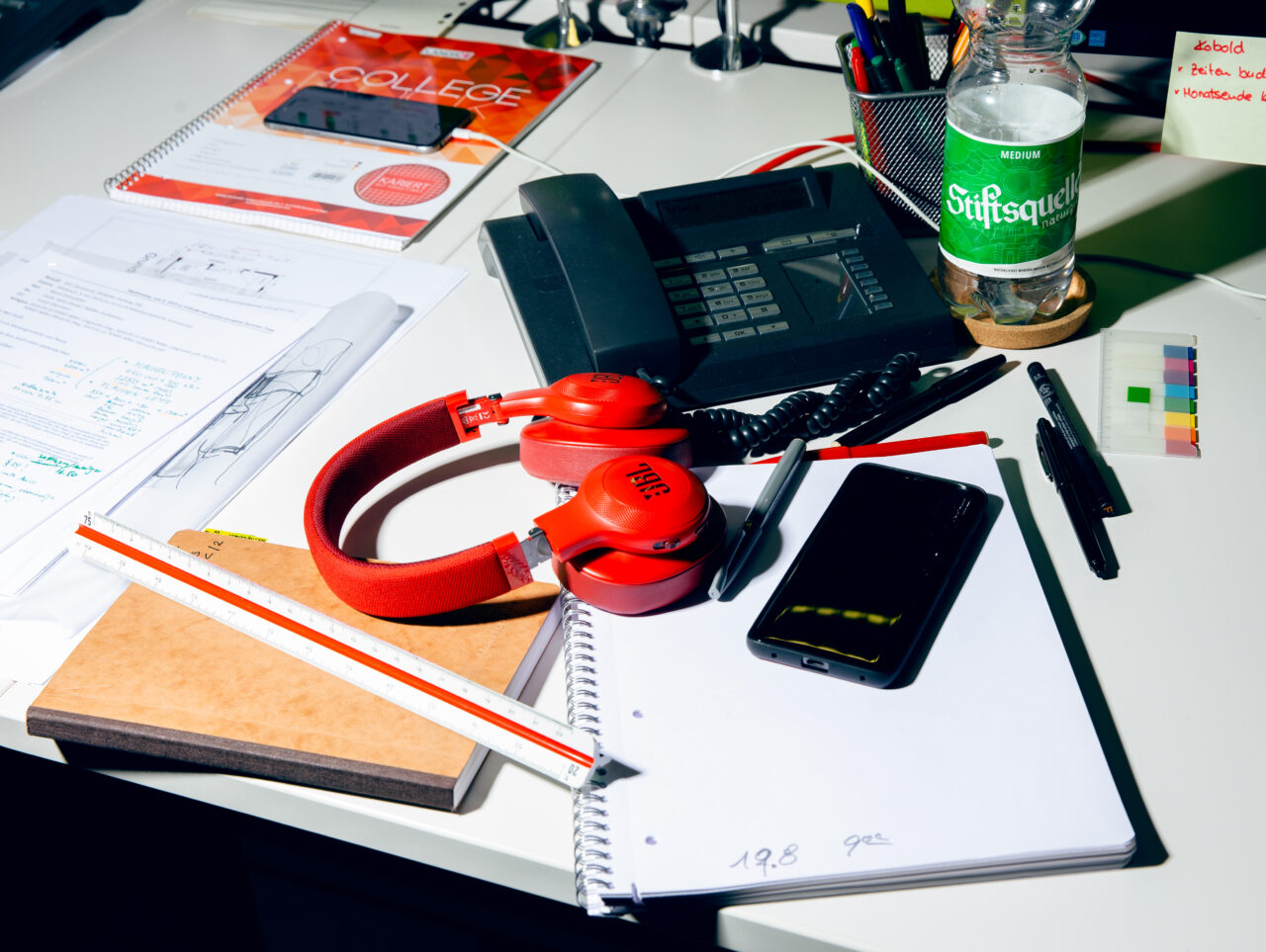 Arbeitsplatz mit Telefon, Unterlagen, Monitor und Kopfhörern als Symbol für die täglichen Anforderungen im Berufsalltag.